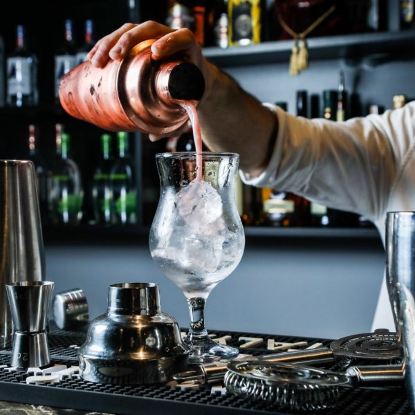 man-pouring-cocktail-from-shaker-in-the-glass-with-ice-bar-side-view.jpg